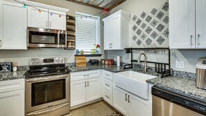 Een keuken met witte kasten, een RVS magnetron, oven en vaatwasser.