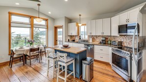 A modern kitchen with a central island, wooden flooring, and a view through the windows. - Hot Tub & Puget Sound View! Whidbey Island Retreat (Clinton)
