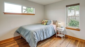 A bedroom with a bed, bedside table, lamp, and two windows. - Hot Tub & Puget Sound View! Whidbey Island Retreat (Clinton)