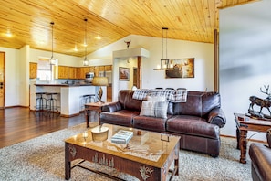 A spacious living room with a leather sofa, a coffee table, and a kitchen in the background. - Torreon Family Retreat, 4BR Mountain Home (Show Low)