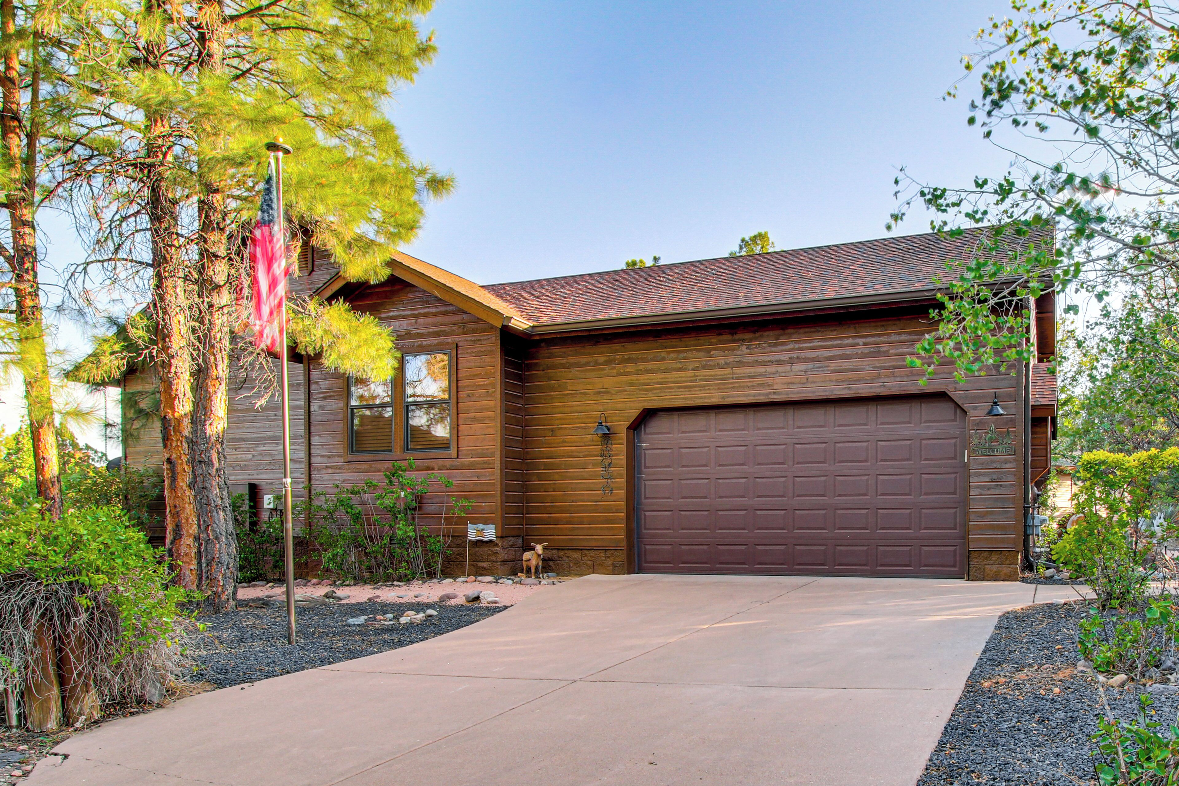 A two-story house with a brown garage door, a flagpole with an American flag, and a well-maintained front yard with trees and shrubs.