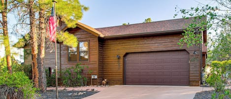 A two-story house with a brown garage door, a flagpole with an American flag, and a well-maintained front yard with trees and shrubs.
