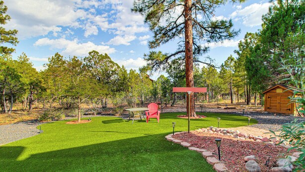 A well-maintained garden with a lawn, a red chair, a wooden shed, and a tall pine tree. - Forests, Fairways & Lake Fun! Show Low Getaway (Show Low)