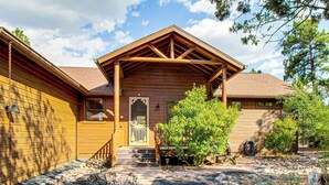 A wooden cabin with a covered porch, a front door, and a small garden with rocks and plants. - Forests, Fairways & Lake Fun! Show Low Getaway (Show Low)