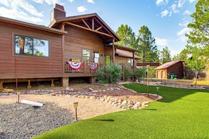 A wooden cabin with a porch, a flag, and a well-maintained garden. - Torreon Family Retreat, 4BR Mountain Home (Show Low)