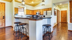A kitchen with wooden cabinets, a stainless steel refrigerator, a microwave, and a coffee maker. There are four stools around the kitchen island. - Forests, Fairways & Lake Fun! Show Low Getaway (Show Low)