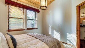 A bedroom with a bed, a window with blinds, a wooden ceiling, and a door leading to a kitchen. - Forests, Fairways & Lake Fun! Show Low Getaway (Show Low)