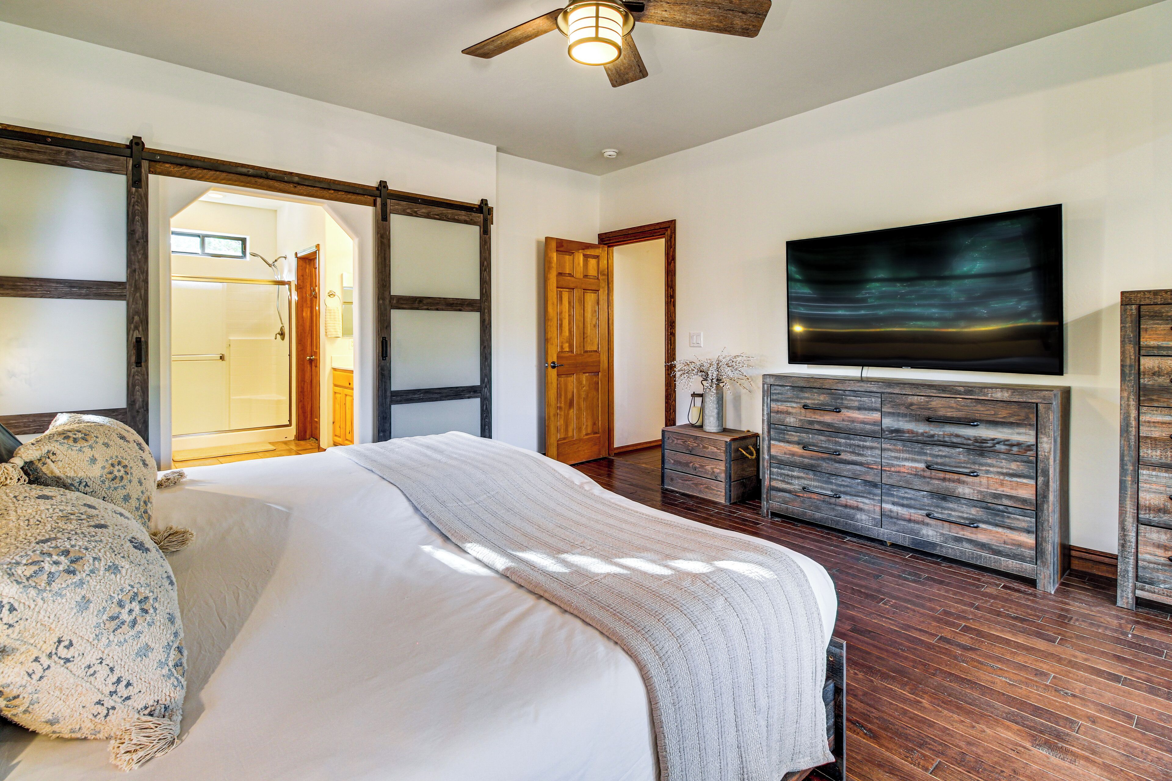 A bedroom with a bed, wooden dresser, and a television on the wall.