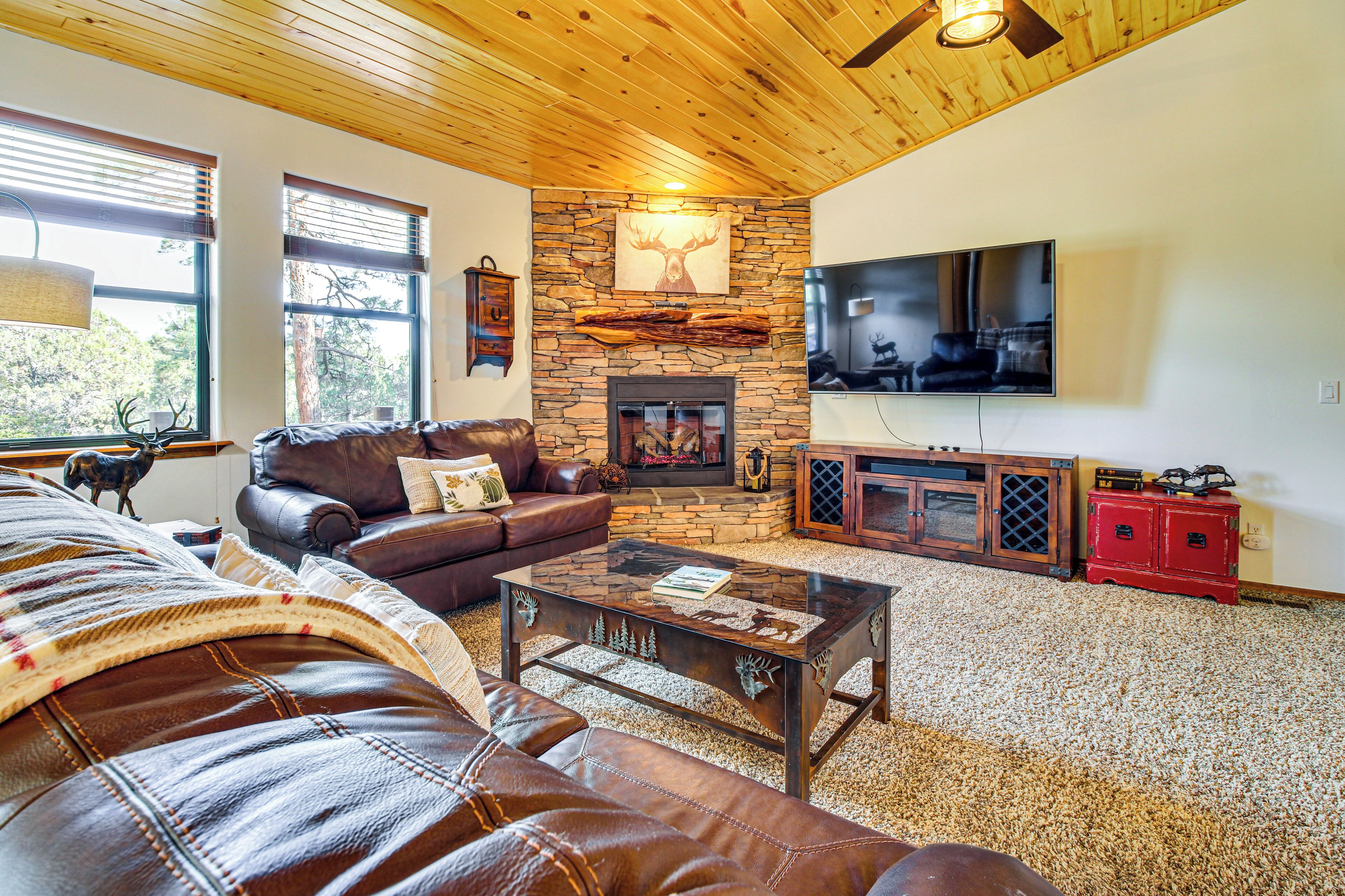A cozy living room with a stone fireplace, leather furniture, a flat-screen TV, and a ceiling fan.