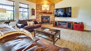 A cozy living room with a stone fireplace, leather furniture, a flat-screen TV, and a ceiling fan. - Forests, Fairways & Lake Fun! Show Low Getaway (Show Low)