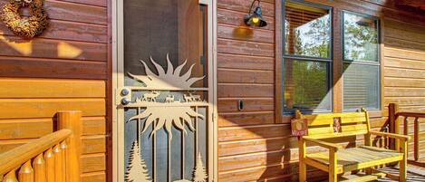 A wooden cabin with a decorative door, a bench, and a welcome mat.