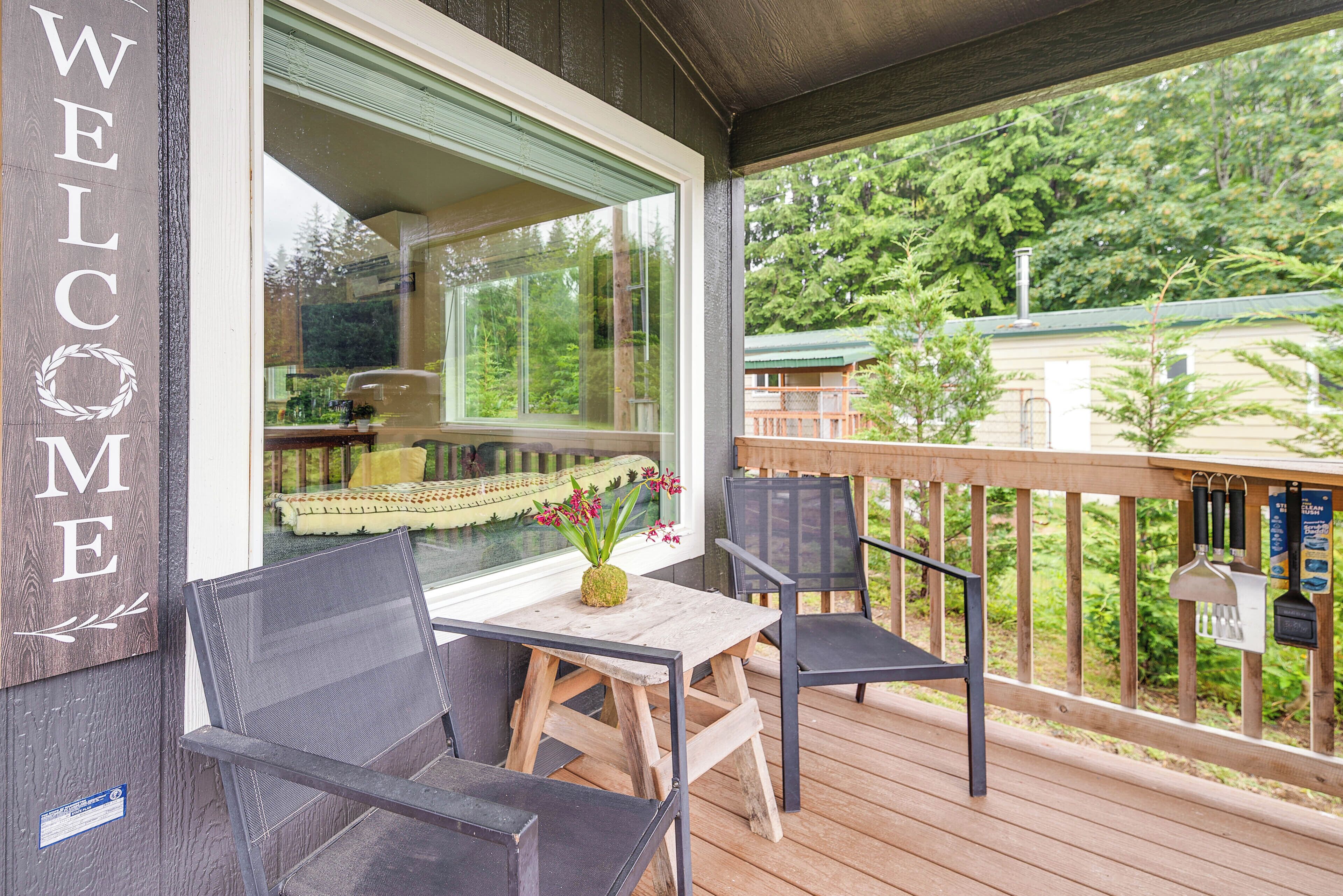 A wooden deck with a 'WELCOME' sign, a table with chairs, and a view of the surrounding greenery.