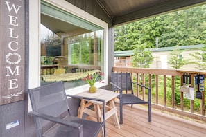 A wooden deck with a 'WELCOME' sign, a table with chairs, and a view of the surrounding greenery. - Walk to Sol Duc River! Cozy Home Near Forks (Beaver)