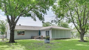 A house with a large tree in the yard, a covered patio, and a small outdoor grill.
