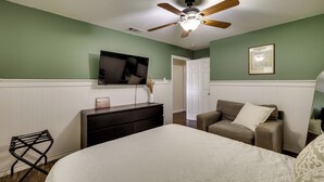 A bedroom with a bed, a dresser, a television, a ceiling fan, and a door.