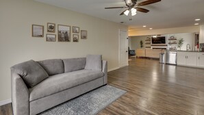 A spacious living area with a grey sofa, wooden flooring, ceiling fan, and framed pictures on the wall. - 4 Mi to Dtwn: Garland Getaway w/ Fenced-in Yard (Garland)