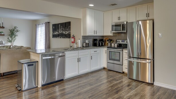A modern kitchen with stainless steel appliances, white cabinetry, and a wooden floor.