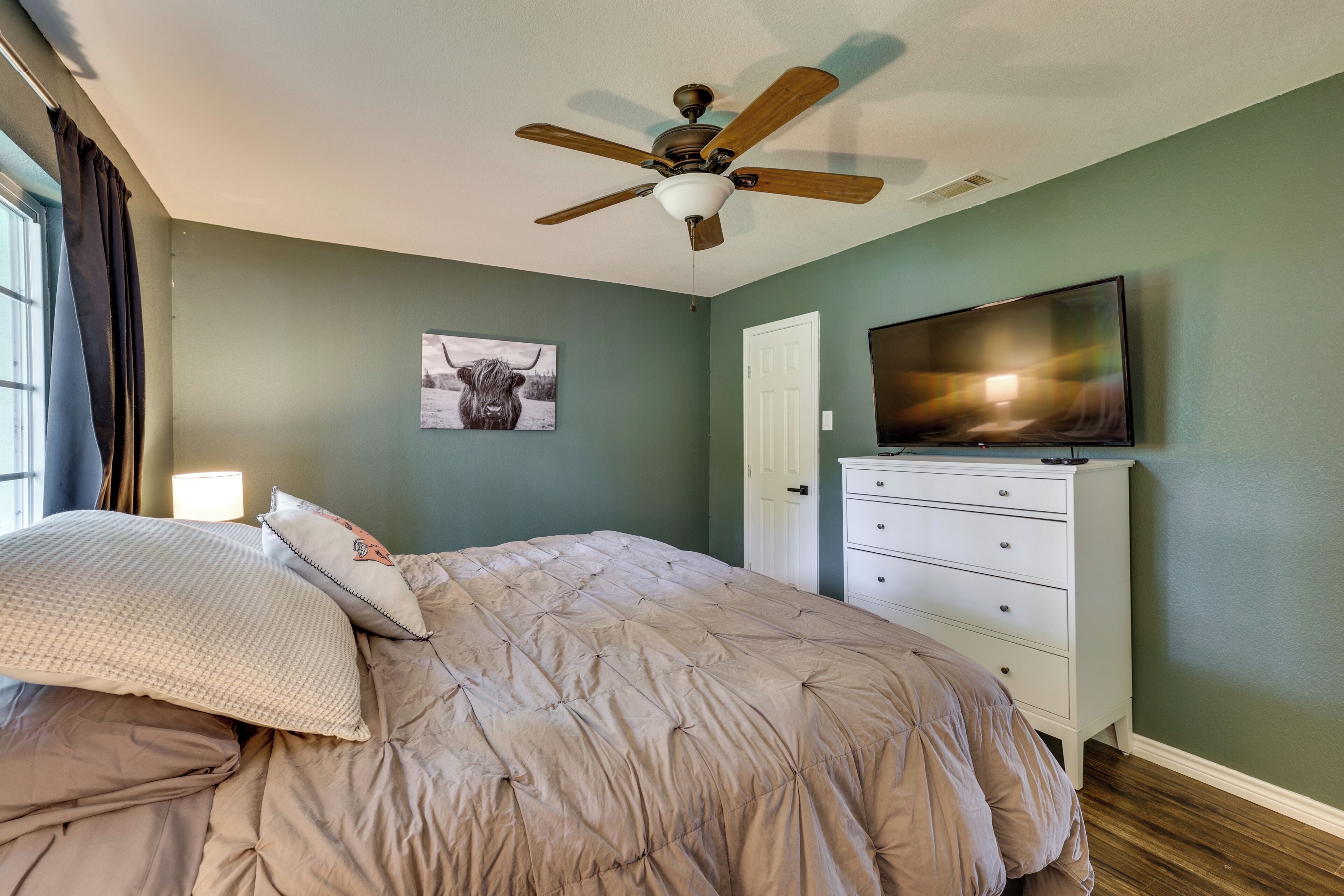 A bedroom with a bed, a ceiling fan, a television, a dresser, and a door.