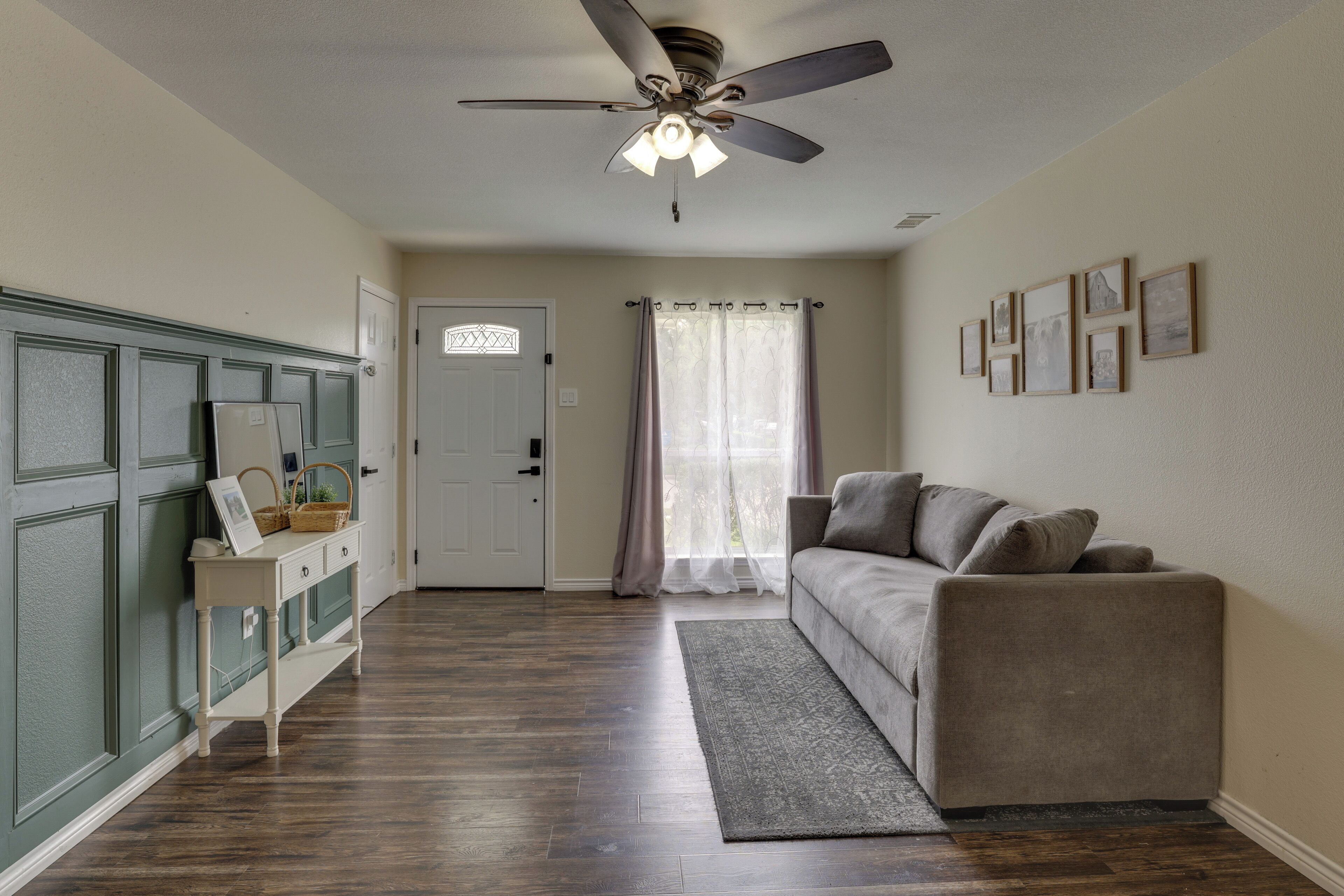 A room with a ceiling fan, a sofa, a console table, and a door with a decorative glass panel.