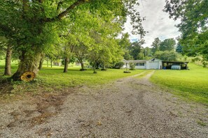 A gravel path leading to a white building with a covered porch, surrounded by trees and a grassy area.