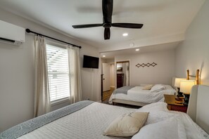 A hotel room with two beds, a ceiling fan, a TV, and a lamp.