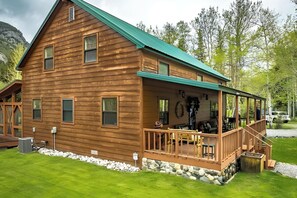 A wooden cabin with a porch, stone foundation, and a vehicle in the background.