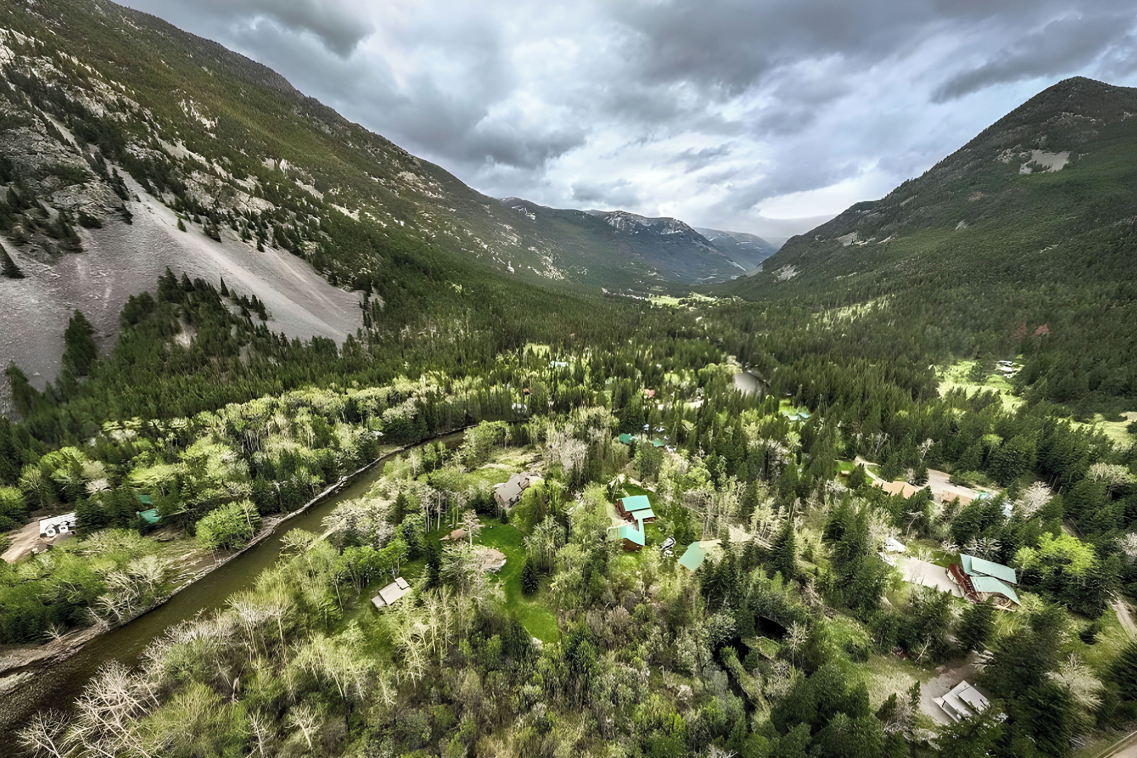 A mountainous landscape with a river, dense forest, and several buildings with green roofs.