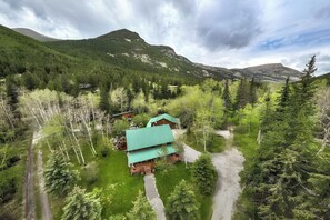 A lodge with a green roof, surrounded by dense forest and mountains.