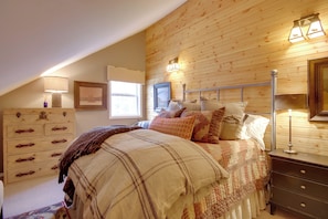 Une chambre avec un plafond en bois, un lit recouvert de plusieurs coussins, une commode et des lampes fixées au mur.