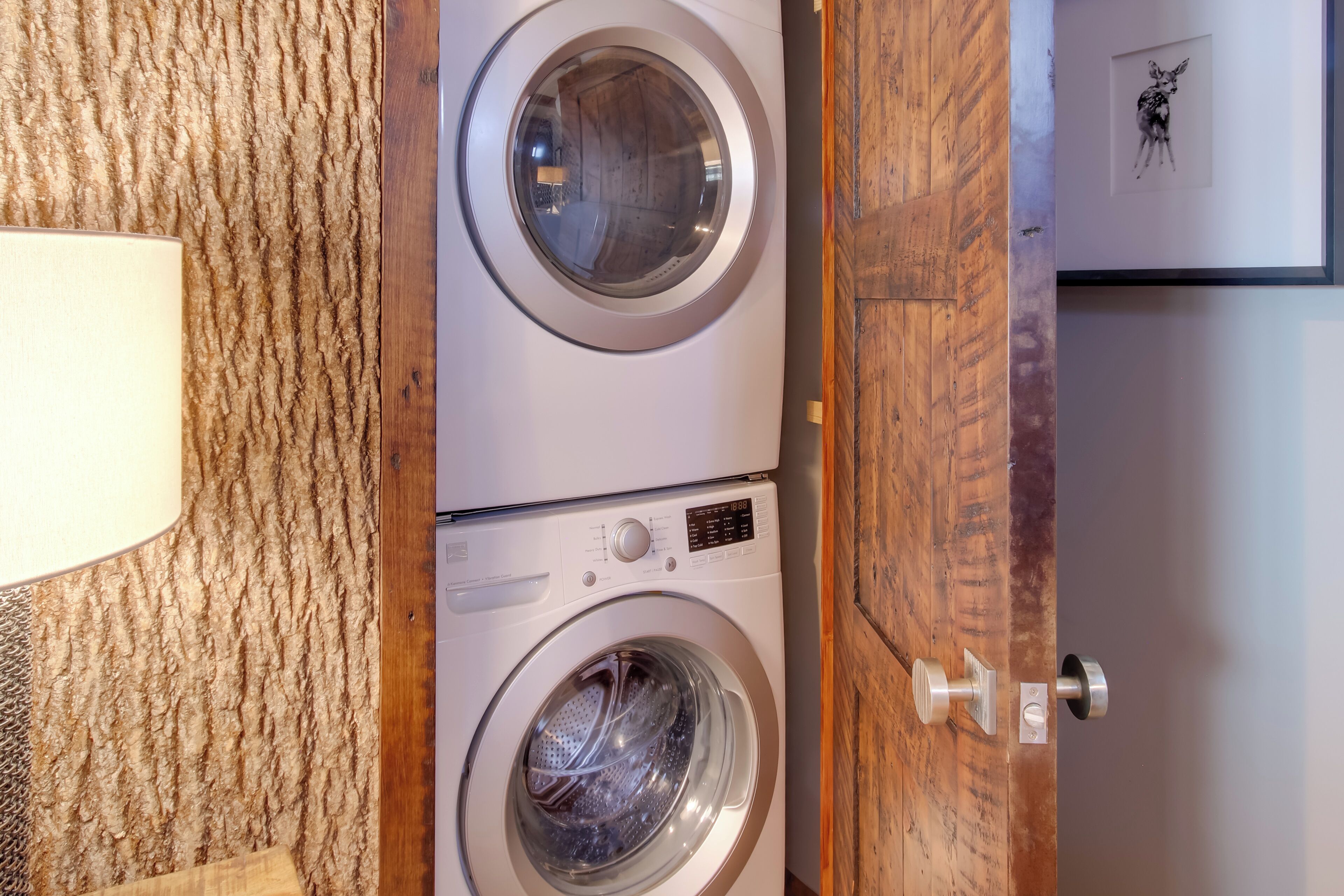 Un cuarto de lavado con dos lavadoras apiladas, una puerta de madera y un cuadro en la pared.
