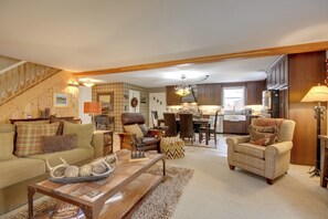A cozy living room with a sofa, armchair, and coffee table, a staircase, and a kitchen in the background. - Great for Families! Woodsy Sanctuary in Mc Leod (McLeod)