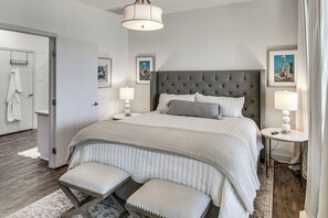 A bedroom with a large bed, bedside lamps, a bedside table, and a door leading to a bathroom. - Modern Lake House With Beautiful Shoreline (Frankston)