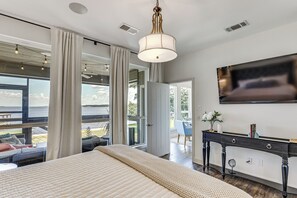 A bedroom with a large bed, a TV mounted on the wall, and a view of the outdoors. - Modern Lake House With Beautiful Shoreline (Frankston)
