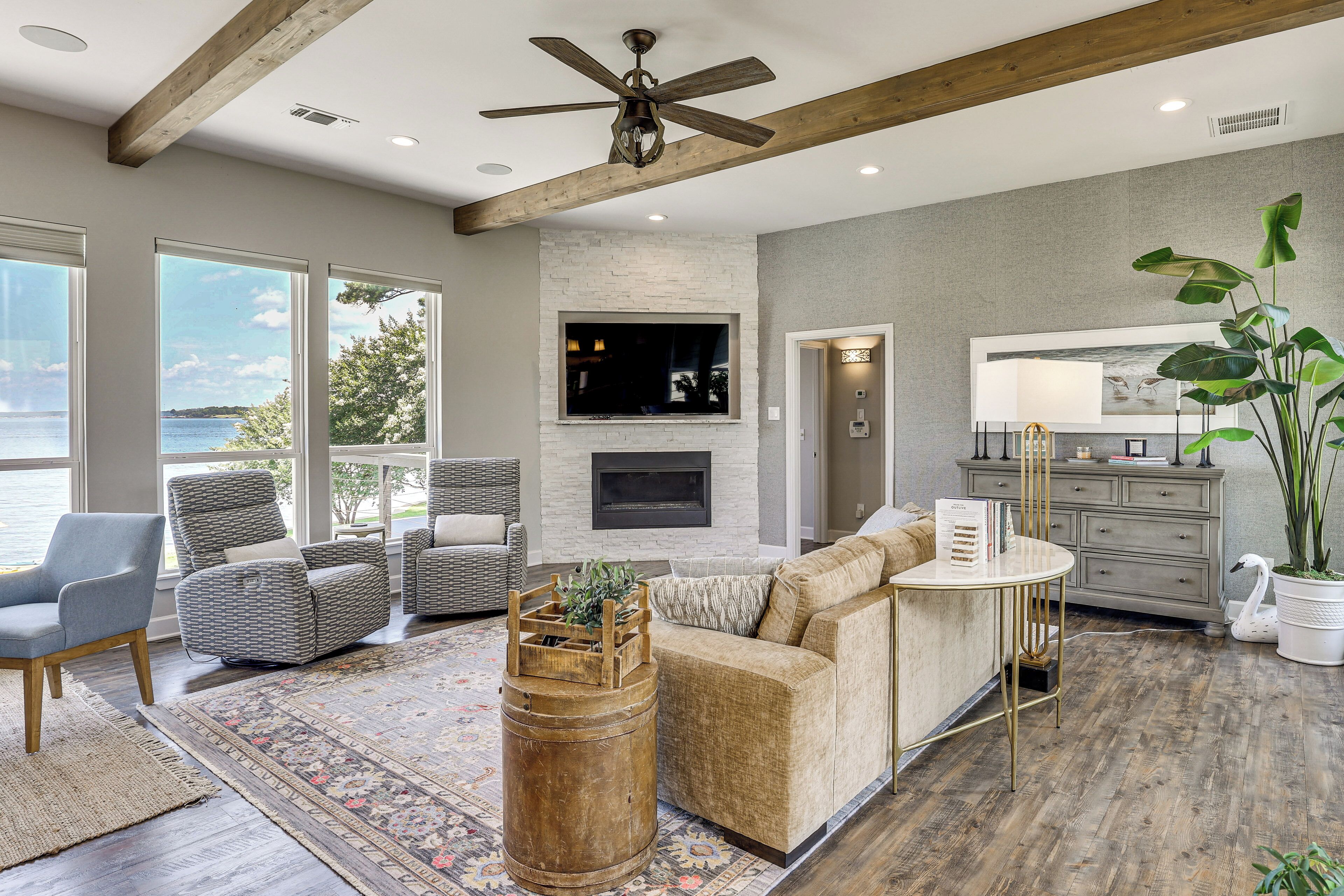 A living room with a fireplace, large windows, and a ceiling fan.