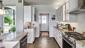 A modern kitchen with white cabinets, a marble countertop, and a gas stove.