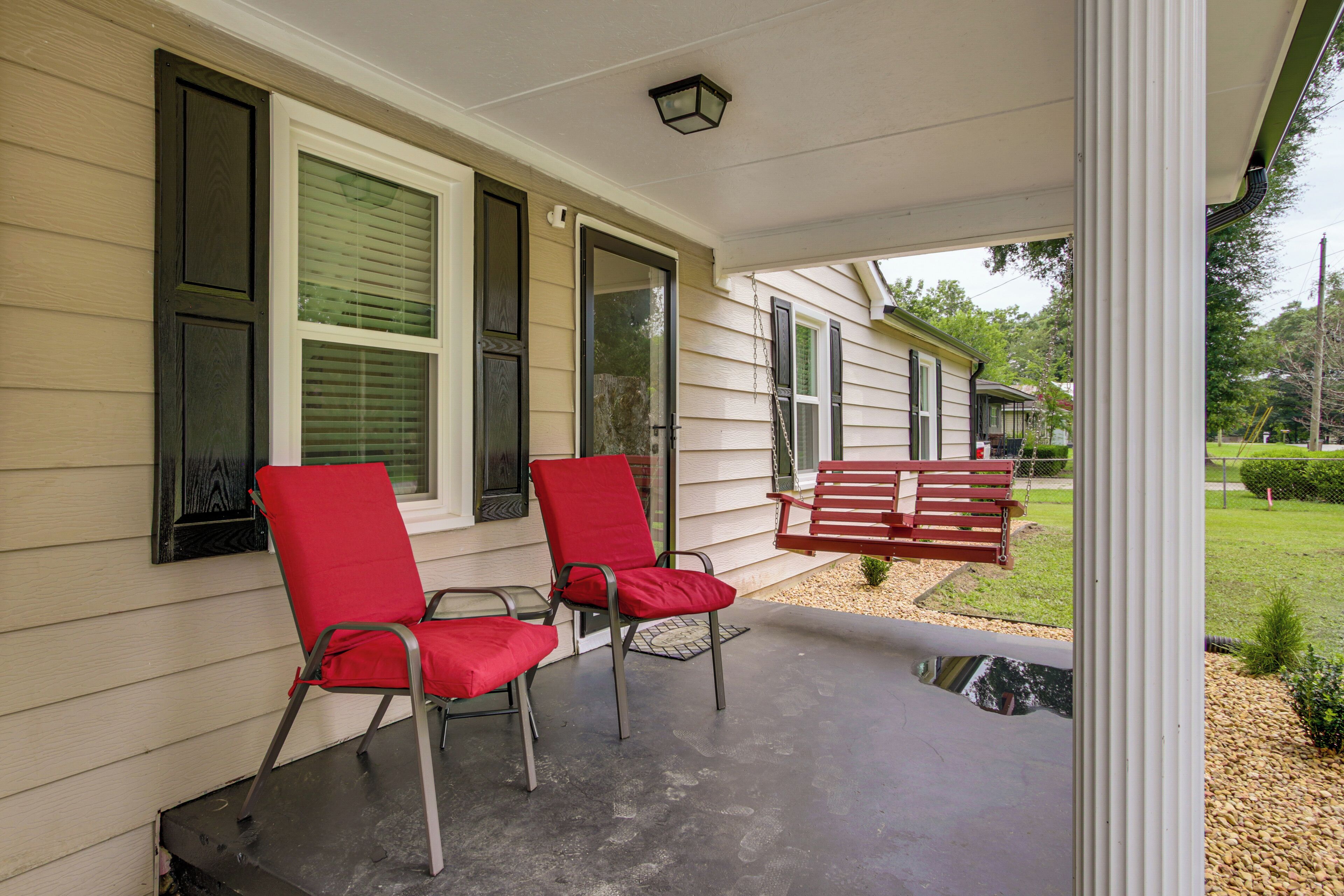 A covered porch with two red chairs and a bench, a window with blinds, and a small garden area.