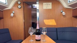 Ein Tisch mit einer Weinflasche und zwei Gläsern, ein Schild mit der Aufschrift 'Welcome aboard Lahor' und eine blau gepolsterte Bank.