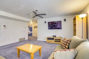 A living room with a ceiling fan, a TV mounted on the wall, a wooden table, a sofa, and a lamp.