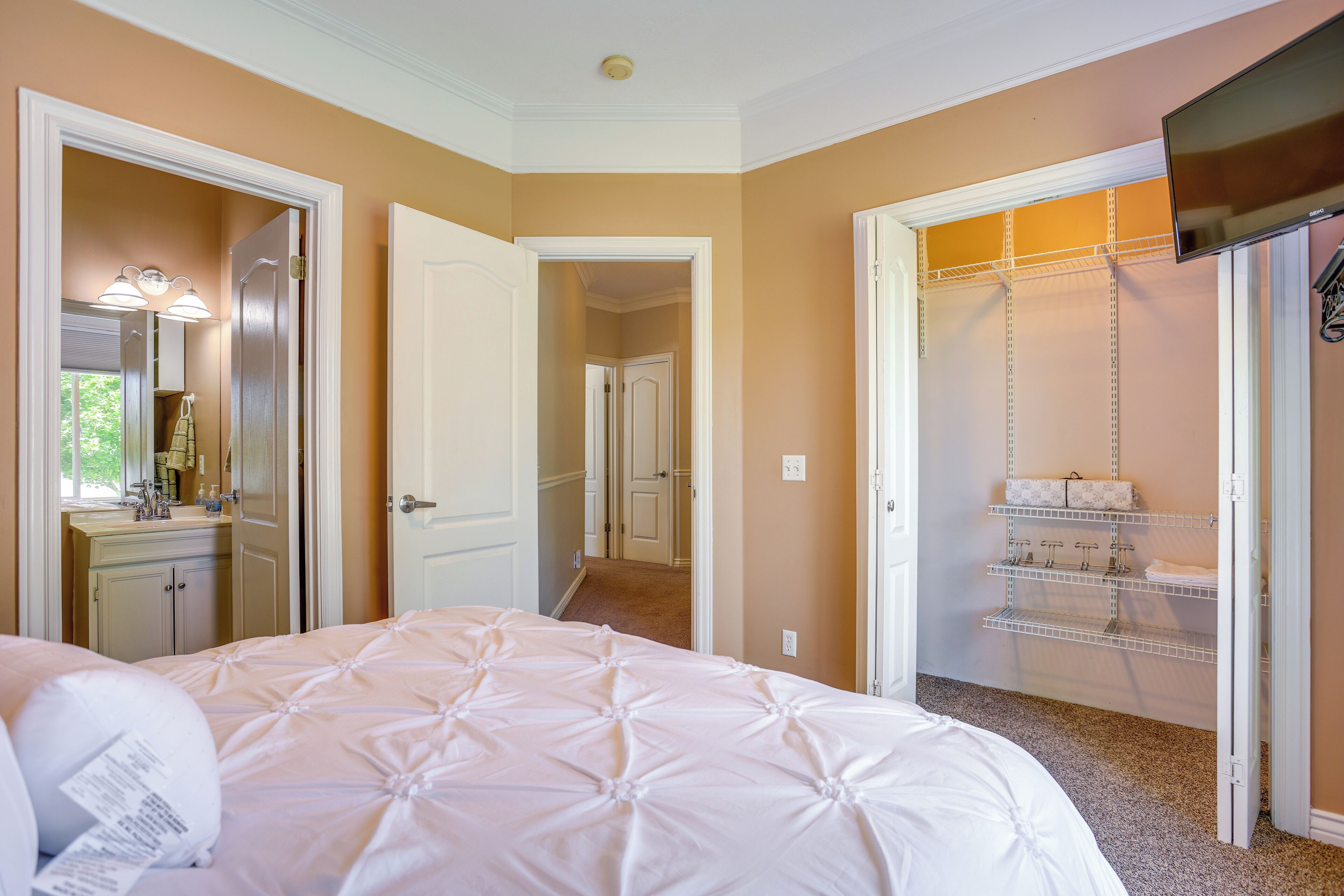 A bedroom with a bed, a walk-in closet, and a bathroom with a sink and mirror.