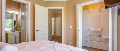 A bedroom with a bed, a walk-in closet, and a bathroom with a sink and mirror.
