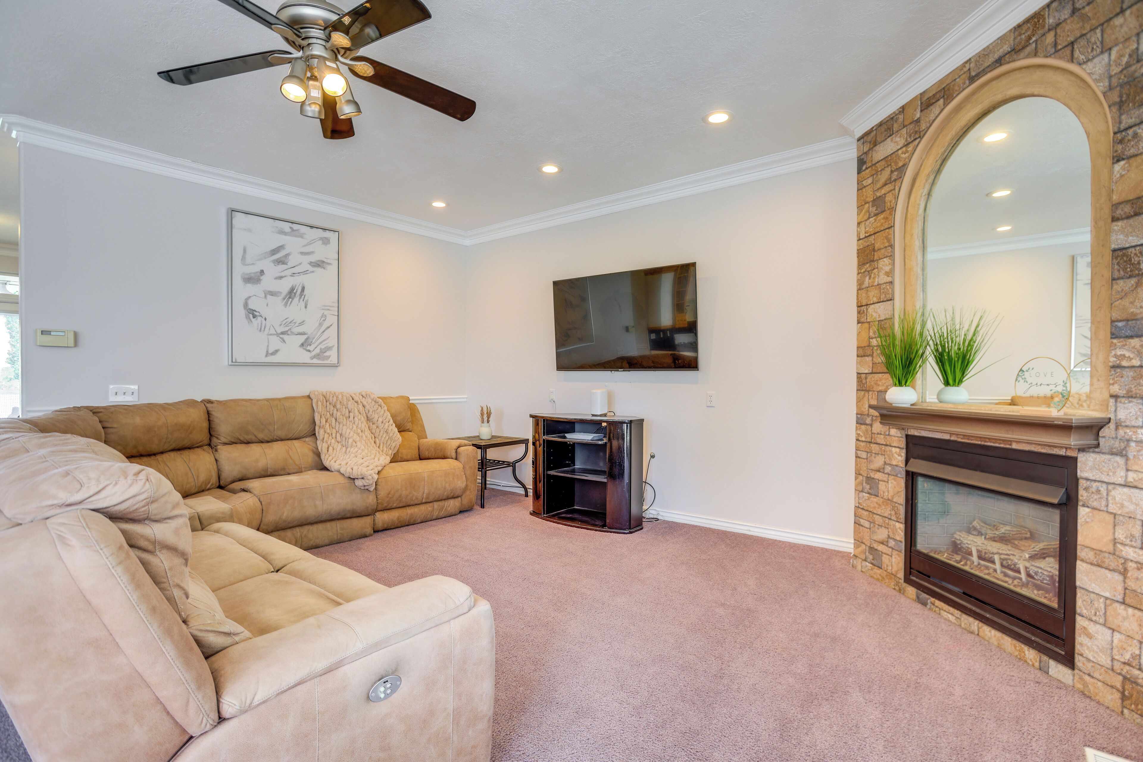 A living room with a sectional sofa, a fireplace, a ceiling fan, and a flat-screen TV.