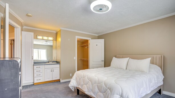 A bedroom with a bed, a walk-in closet, a bathroom with a mirror, and a ceiling fan. - Near Hill Afb! Dual-unit Home w/ Deck & Patio (Clearfield)