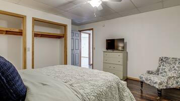 A bedroom with a bed, a dresser, a chair, a ceiling fan, and a door leading to another room.