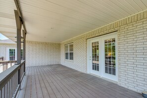 A covered porch with a brick wall, wooden floor, and a white door with glass panels.