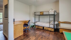 Ein Stockbett mit Schreibtisch und Stuhl, ein kleiner Tisch und ein Deckenventilator in einem Zimmer mit Holzboden.