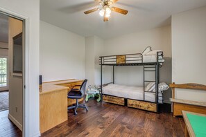 Ein Stockbett mit Schreibtisch und Stuhl, ein kleiner Tisch und ein Deckenventilator in einem Zimmer mit Holzboden.