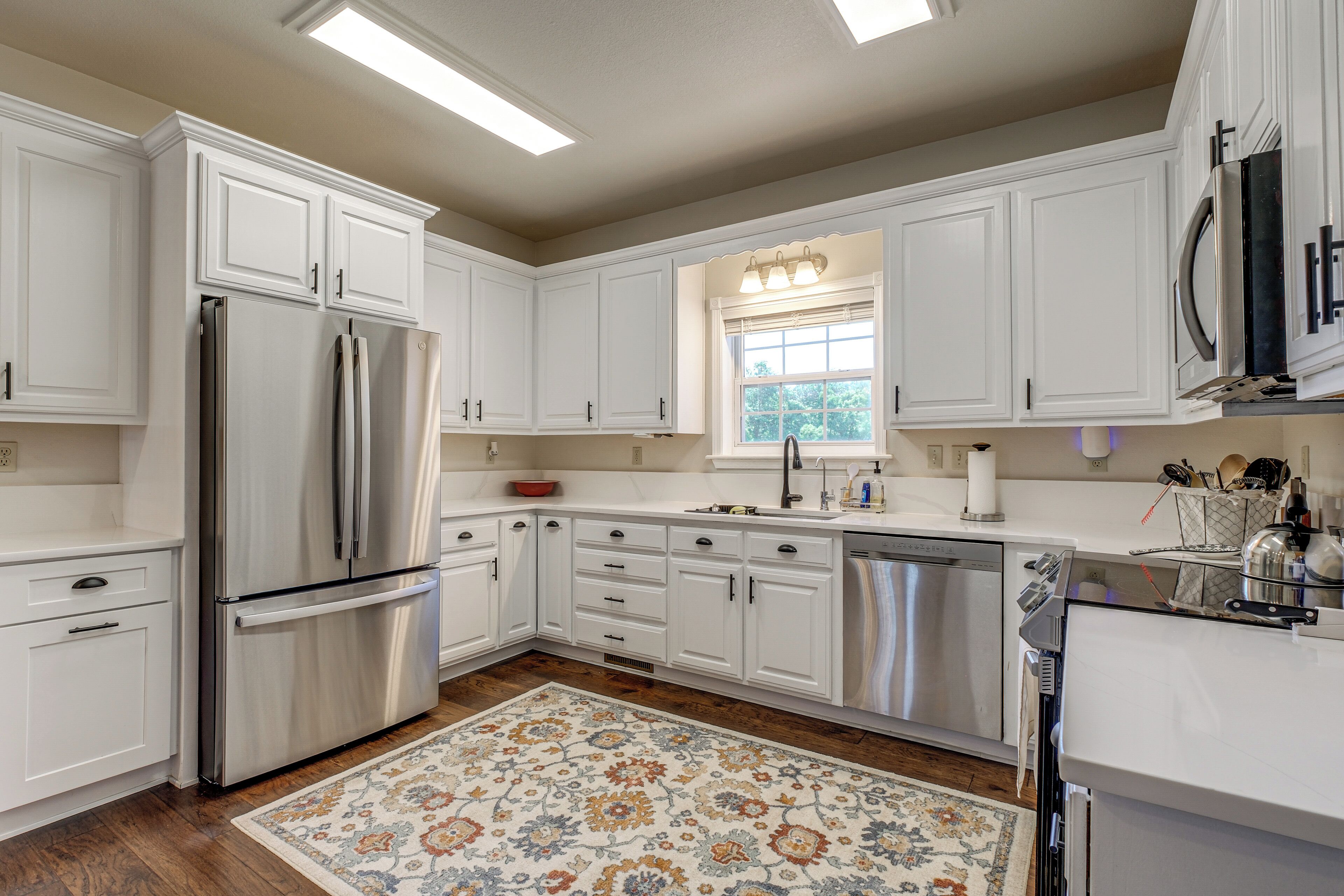 A modern kitchen with white cabinetry, stainless steel appliances, and a patterned rug.