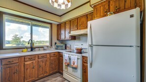 A kitchen with wooden cabinets, a white refrigerator, a stove, and a window with a view of trees. - Peaceful Fulton Farm Retreat w/ Outdoor Space! (Fulton)
