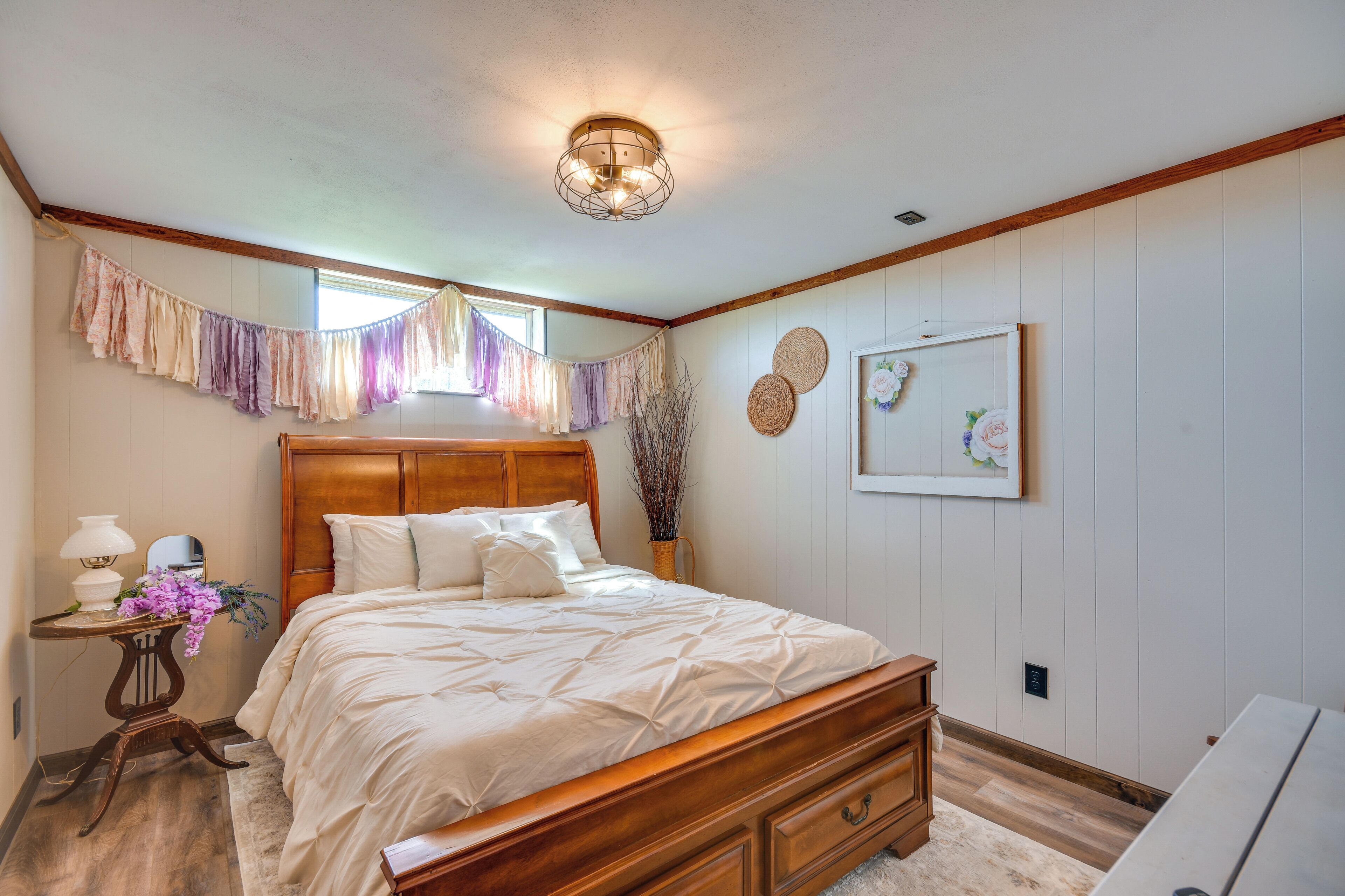 Un dormitorio con cama de madera, una mesita de noche con lámpara y una ventana con cortinas.