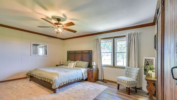 A bedroom with a bed, a chair, a nightstand, a window with curtains, and a ceiling fan. - Peaceful Fulton Farm Retreat w/ Outdoor Space! (Fulton)